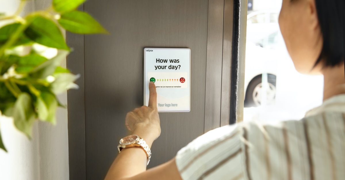 Woman using tablet on the wall. Tablet is asking how the person's day was with the option to select a level of satisfaction from happy to sad.